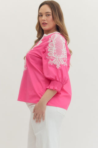 Woman wearing a pink blouse with white lace embroidery on a plain background