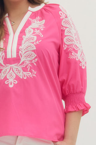 Pink top with white lace detailing on a plain background