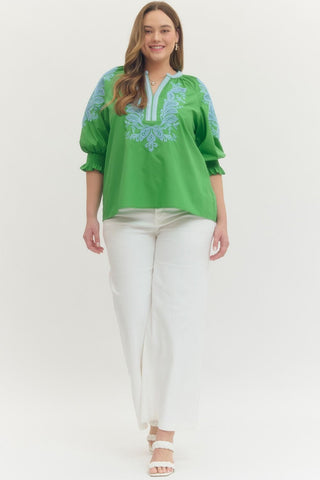 Woman wearing a green embroidered blouse and white pants on a white background