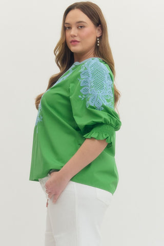 Woman wearing a green blouse with blue embroidery on a white background