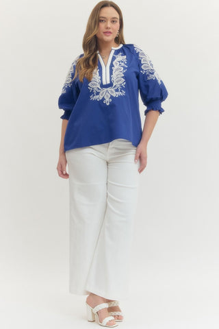 Woman wearing a blue embroidered blouse and white pants on a white background