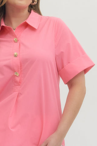 Close-up of a person wearing a pink short-sleeve shirt with gold buttons on a light gray background