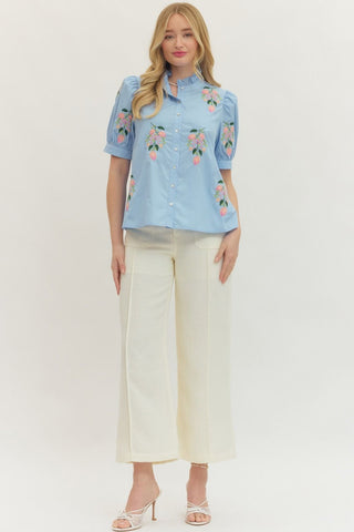 Woman wearing a light blue floral blouse and white pants on a white background