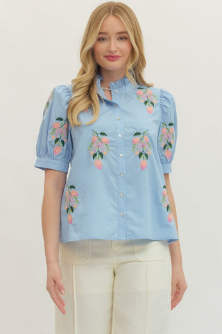 Woman wearing a light blue blouse with floral embroidery on a plain background