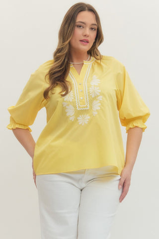 Woman wearing a yellow blouse with white embroidery on a plain background