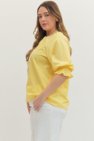 Woman wearing a yellow blouse with ruffled sleeves against a white background