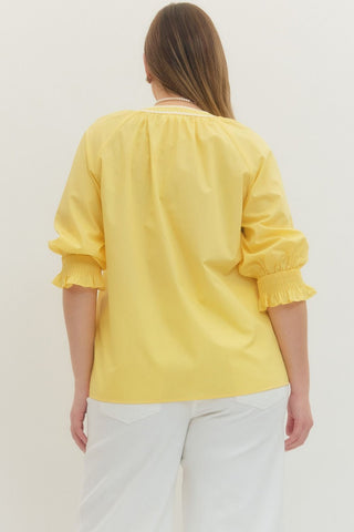 Person wearing a yellow blouse with white pants on a plain background