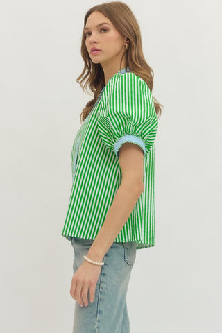 Woman wearing a green and white striped shirt with blue trim on a plain background