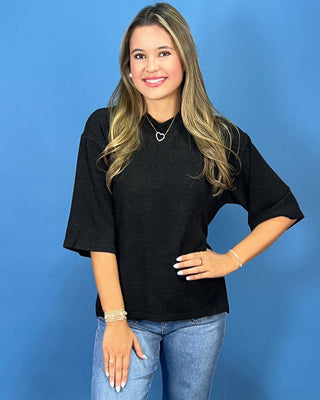 A woman modeling a black short-sleeve mock neck top with blue jeans and metallic shoes