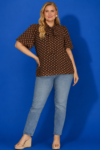 Woman wearing a brown polka dot blouse and blue jeans against a blue background