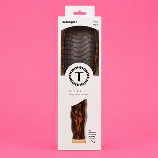 Packaging of a hair detangler with tortoiseshell design on a pink background