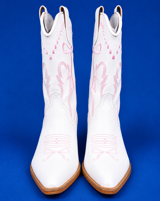 A pair of white leather cowboy boots with pink embroidered western-style patterns, shown against a solid blue background.