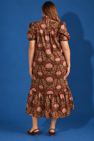 A woman viewed from the back wearing a brown midi dress with puff sleeves and an allover floral pattern in pink, orange, and beige