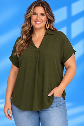 A woman wearing an olive green short-sleeve collared blouse with a V-neck and gathered front detail, paired with light blue jean