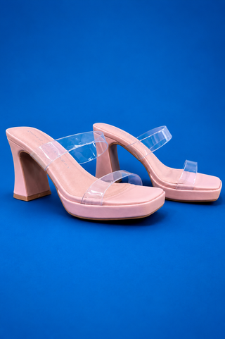A pair of pink platform mule sandals with clear plastic straps and block heels, displayed on a solid blue background.