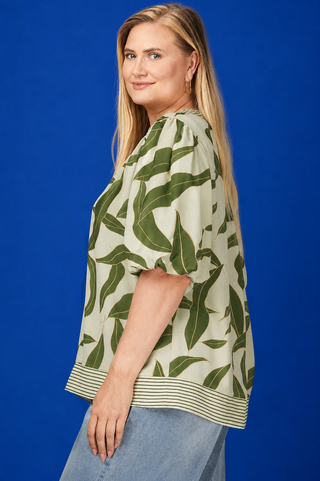 Woman wearing a green leaf-patterned top against a blue background