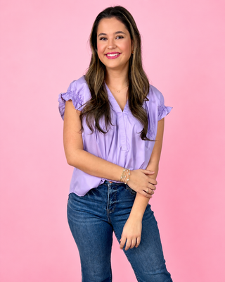Woman wearing a purple blouse and blue jeans against a pink background