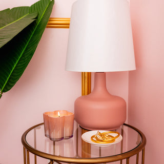Pink lamp on a glass table with a candle and plate against a pink wall.