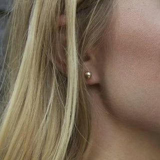 eNewton Classic Gold Ball Stud Earrings featuring polished gold-filled ball studs with secure post backs, minimalist everyday earrings shown on a jewelry card and worn in an ear piercing.