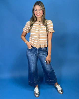 A woman modeling a beige and white striped short-sleeve top with ruffle details, paired with wide-leg blue jeans and white sn