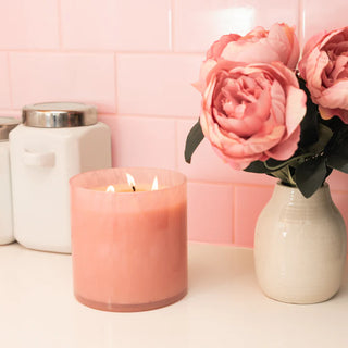 Pink candle and vase with flowers on a pink tiled wall background
