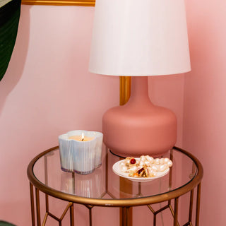 Round glass table with a pink lamp, candle, and decorative items against a pink wall.