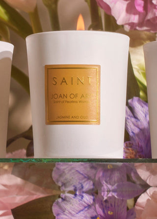 White candle with a gold label reading 'Saint Joan of Arc' against a floral background