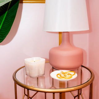 Pink lamp on a glass table with a candle and plate against a pink wall