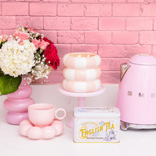 Pink tea set with flowers and a toaster against a pink brick wall.