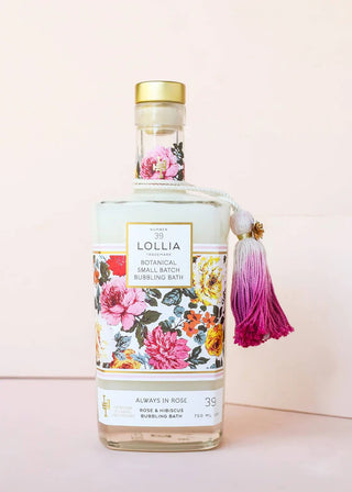 Bottle of Lollia bubbling bath with floral design and tassel on a light pink background