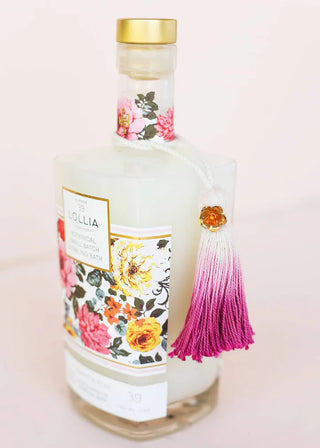 Decorative bottle with floral label and pink tassel on a light pink background