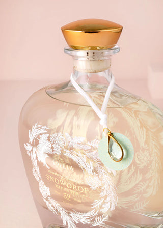 Glass bottle with gold cap and decorative label on a pink background