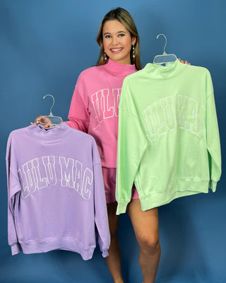 A woman modeling a bright pink two-piece lounge set consisting of a sweatshirt and matching shorts
