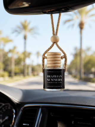 A car diffuser bottle hanging from the rearview mirror inside a car, with a blurred outdoor background of palm tree