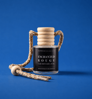 A car diffuser bottle with a dark charcoal label reading 'ENCHANTED ROUGE' and a natural wood reed diffuser on to