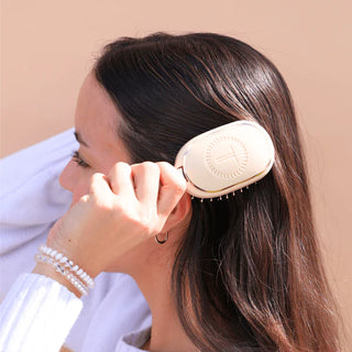 Person using a beige hairbrush on their hair against a beige background