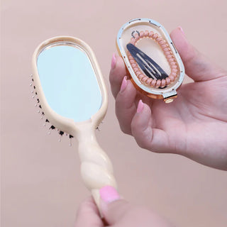 Hairbrush with mirror and hair removal tool on a pink background