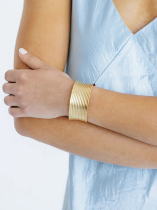 Gold bracelet on a person's wrist with a light blue top