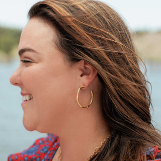 Woman wearing gold hoop earrings with a blurred natural background