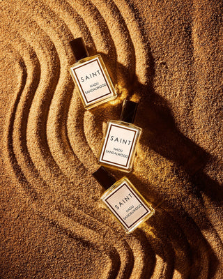 Three 'SAINT' perfume bottles on sand with ripples