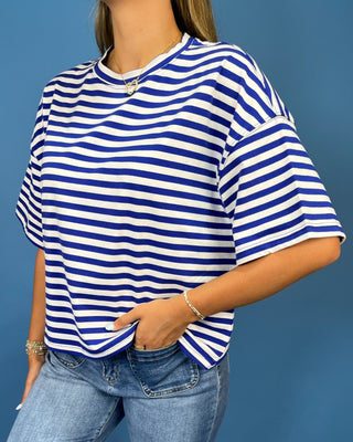 A woman wearing a blue and white horizontally striped short-sleeve t-shirt with light wash blue jeans, standing against a so