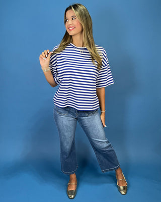 A woman modeling a navy and white horizontally striped short-sleeve t-shirt, paired with blue jeans and metallic gold flats,