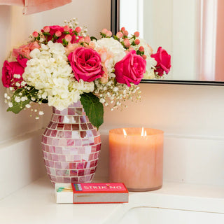 Decorative vase with pink and white flowers and a candle on a shelf.