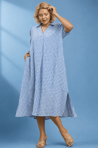 A woman modeling a light blue and white gingham midi dress with short sleeves, a V-neck, and side pockets