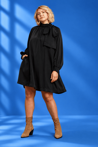 A woman modeling a black long-sleeve mini dress with a large bow at the neck
