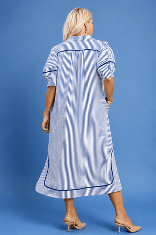 A woman viewed from the back wearing a blue and white vertically striped midi dress with dark blue piping details