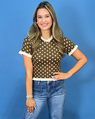 a brown short-sleeve top with white polka dots and white lace trim at the collar and cuffs,