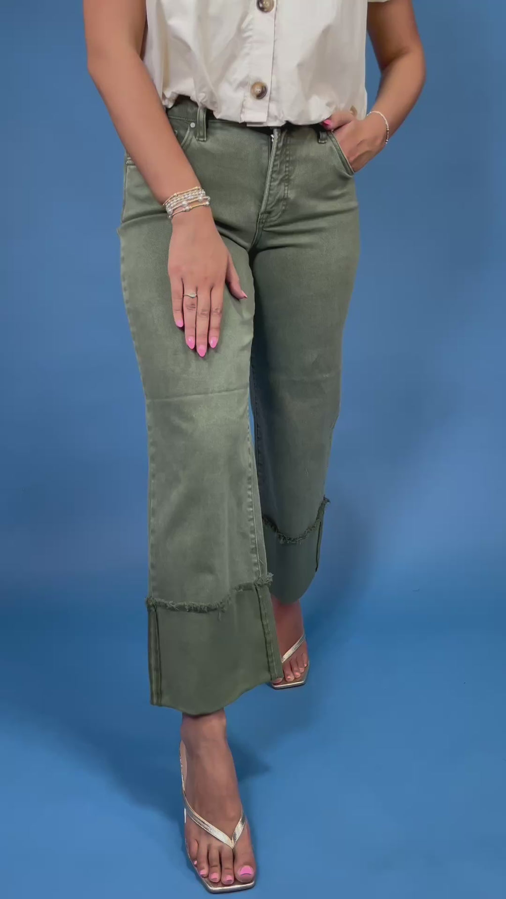 A model wearing a pair of olive green wide-leg cropped jeans with rolled cuffs, paired with a white blouse