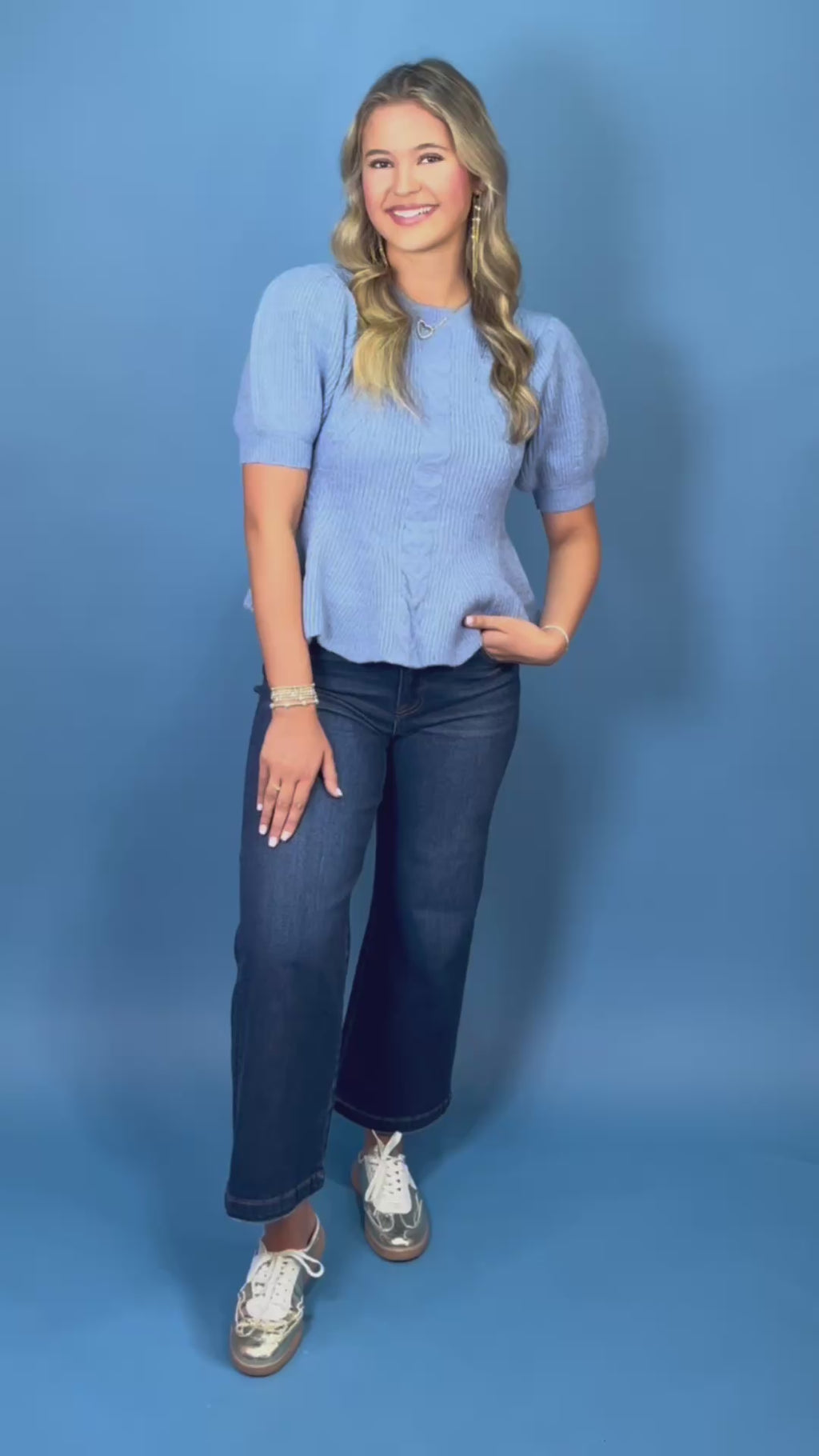 Woman modeling a light blue cable knit puff sleeve peplum sweater top with dark wash wide leg jeans.