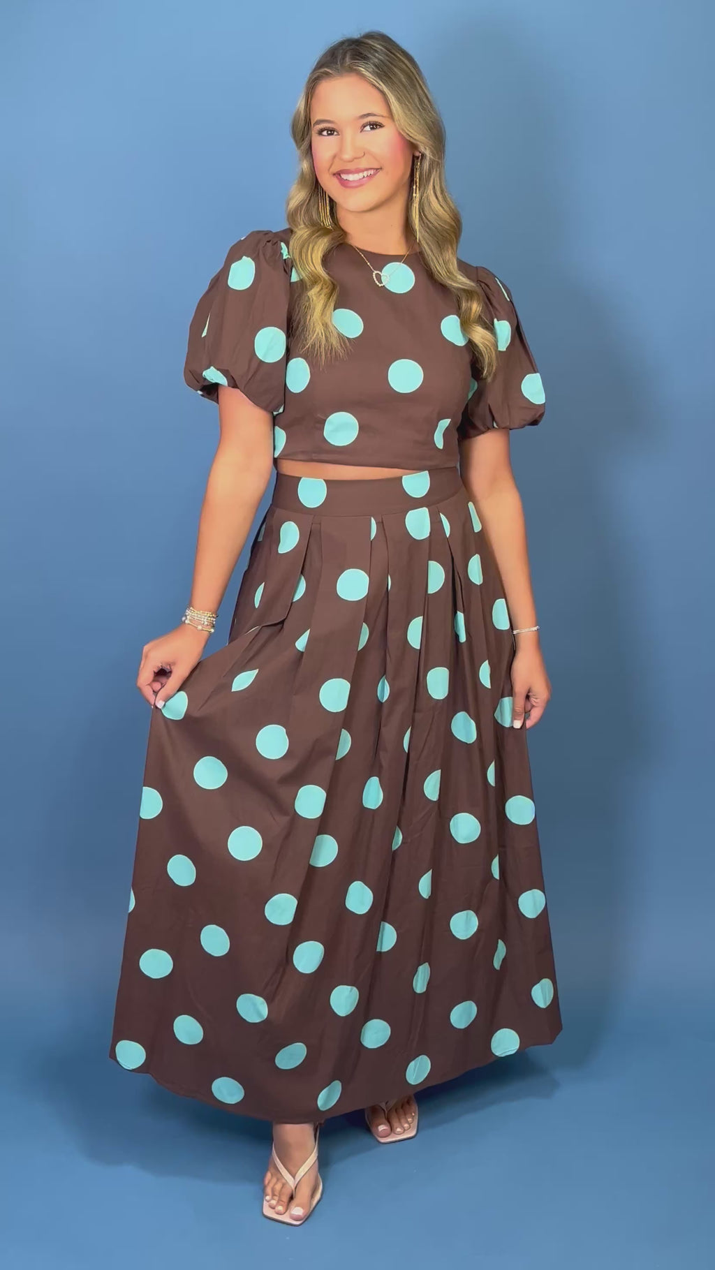 Woman modeling a brown and turquoise polka dot puff sleeve crop top with a matching pleated maxi skirt.